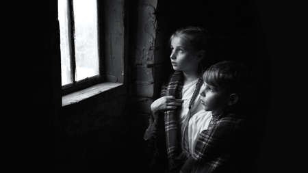 Cute happy little worry pretty femal pauper waif human hand help face eye see warm hope dream life. Rural dirty dark cold old house room wall stand small misery teen fear grief talk concept text spaceの写真素材