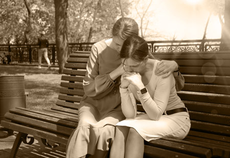 2 young adult lady sit hand talk old urban summer city town garden tree. Teen youth bad feel guilty...