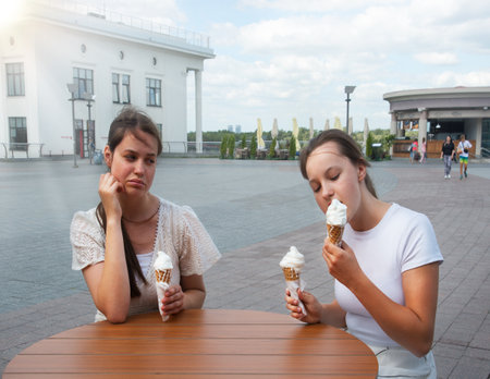 2 young teen joy cheer fun lady kid child sit frown greed sweet tasty fast meal diet sad angry quarrel skeptic doubter think funny bad mad moody judg emot habit problem parkの写真素材