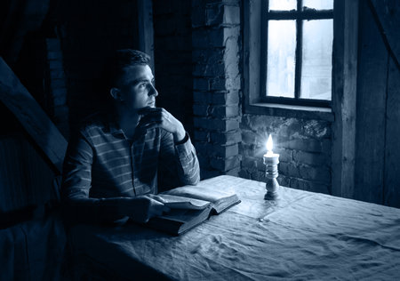 Young alone love hope human face sacred divin Jesus seat look teach open holy page note word. Antique israeli sad lone male guy boy student sit dark black fire flame light table church home room spaceの写真素材