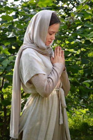 Lone holy young sad east jew Mary old retro shawl veil kneel park lawn hand think ask beg wish Lord Jesus Christ. Rural village teen child kid lady happy joy face thank praise trust peace sun lightの写真素材