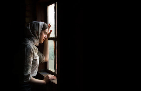 Orthodox adult lone worry fail poor holy lady trust ask plead god peace love old Ukraine history. Cold war young human teen face think life dark home room text space look light skyの写真素材