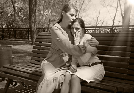 2 young adult lady sit hand talk old urban summer city town garden tree. Teen youth bad feel guilty...
