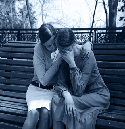 2 young adult lady sit hand talk old urban summer city town garden tree. Teen youth bad feel guilty...