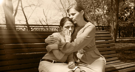 2 young adult lady sit hand talk old urban summer city town garden tree. Teen youth bad feel guilty shame offend think lost love mourn grief pain mood sunny outside nature tell advice pray god faithの写真素材