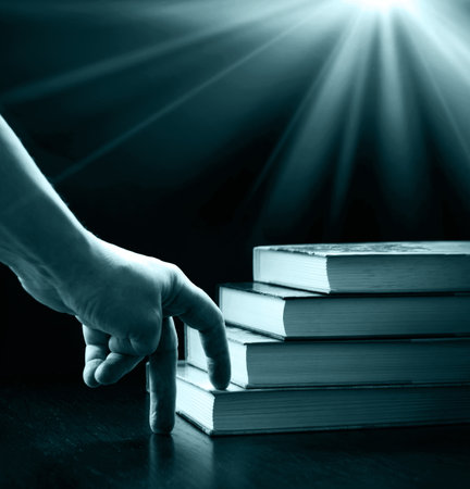 Closeup view of a hand reaching for a stack of books on a desk.の写真素材