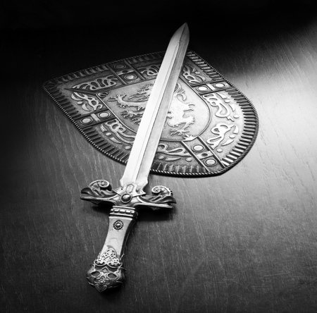 Close up sharp black iron sabre hilt handle power brave male wood table text space Past king middle age rome legion man hero lion sign icon defenc emblem gold roman cross crest coat art banner patternの写真素材