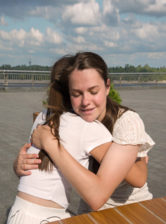 2 young adult lady sit hold arm hand cry talk urban sunny outside summer city town lake cafe table. Teen youth good feel sad failure stress upset grief pain mood tell joy cheer trust god faith crisisの写真素材