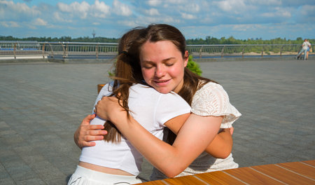 2 young adult lady sit hold arm hand cry talk urban sunny outside summer city town lake cafe table. Teen youth good feel sad failure stress upset grief pain mood tell joy cheer trust god faith crisisの写真素材