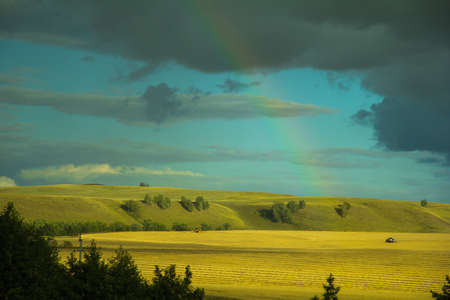 Rainbow in the field and two combine-harvesterの写真素材