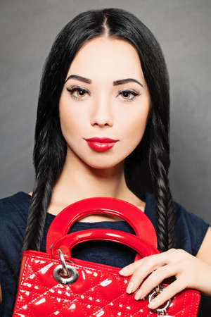 Portrait of a beautiful brunette woman with red handbag in her hand.の写真素材