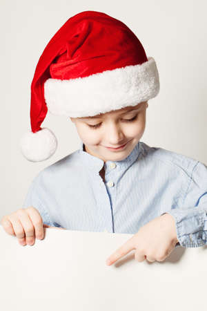 Little Boy Wearing Santa Hat Point the Finger at White Bannerの写真素材