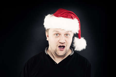 Surprised Man Open his Mouth in Santa Hat on Dark Backgroundの写真素材