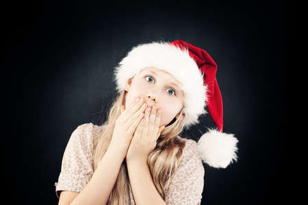 Christmas Surprised Girl in Santa Hat on Dark Backgroundの写真素材