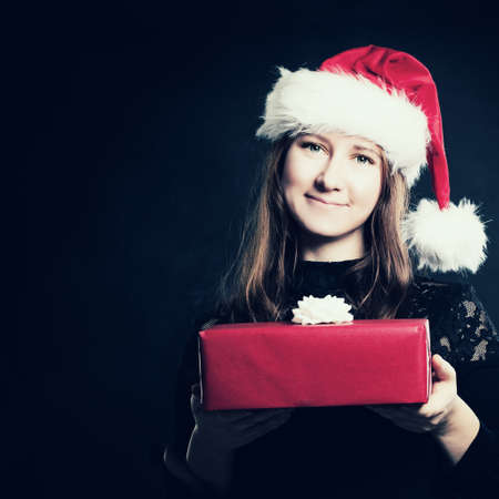 Christmas Woman in Santa Hat with Red Gift Box on Dark Backgroundの写真素材