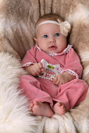 Sweet beautiful baby girl lying in a fur seatの写真素材