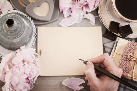 Blank Paper, Coffee, Male Hand with Pen, Post Cards and Peony Flowers on Rustic Wooden Tableの写真素材