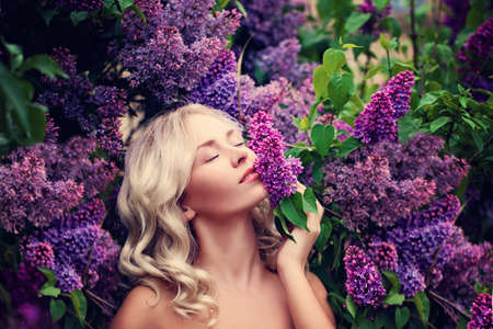 Beautiful Woman Enjoying the Smell of Lilac. Cute Model and Flowers. Aromatherapy and Spring Conceptの写真素材