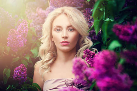 Romantic Woman with Summer Light and Lilac Flowers Outdoors. Young Beauty in Sunny Flowers Gardenの写真素材