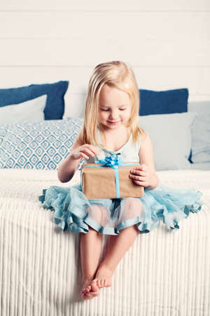Cute Child Girl Opening Gift with Blue Ribbon at Home. Child with Gift Boxの写真素材