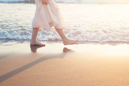 White Skirt Woman Legs Walking on Beach Vacation. Closeup of Barefoot Female Young Adult Lower Body Relaxing in Ocean Water on Summer Holiday Travelの写真素材