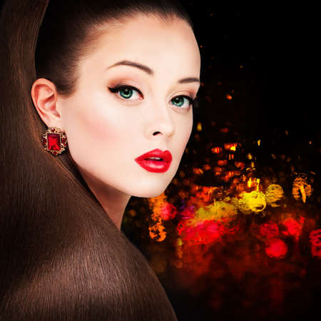 Glamorous Woman Fashion Model with Long Hairstyle, Red Lips Makeup and Earrings on Night Party Backgroundの写真素材