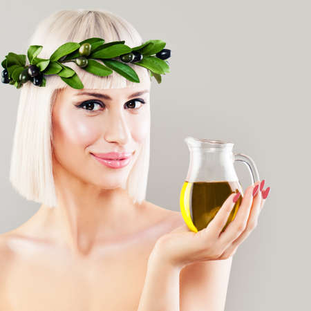 Beautiful Woman with Green Olive Leaves Wreath and Glass Bottle of Organic Olive Oil. Healthy Eating and Mediterranean Diet Conceptの写真素材
