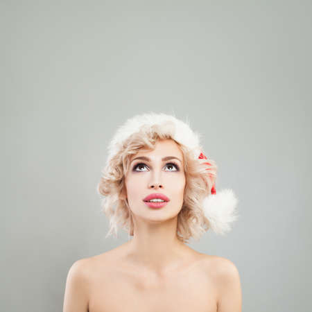 Cute Christmas Woman Looking Up on Gray Background. Pretty Girl in Santa Hatの写真素材