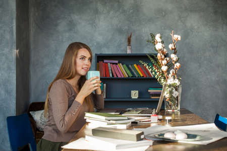 Cute Woman Sitting in Office, Drinking Coffee and Using Laptopの写真素材