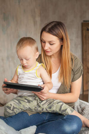Mother and son sitting on sofa using digital tablet. Mom and little boy using tablet with touchscreen together watching a videoの写真素材