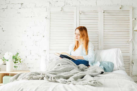 Attractive Redhead Woman with Book at Home with Grey Knitted Woolen Plaidの写真素材