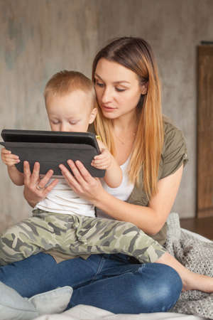 Young mother helping her son with digital tablet at home.の写真素材