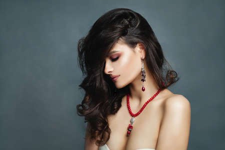 Beautiful Brunette Woman Fashion Model with Healthy Curly Hairstyle, Red Necklace and Earrings on Blue Background with Copy spaceの写真素材