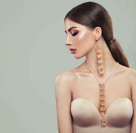 Fashionable Brunette Model with Gold Jewelry. Young Woman with Ponytail Hairstyle, Necklace and Earringsの写真素材