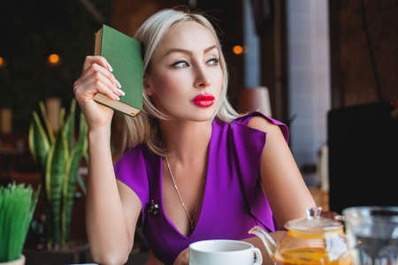 Beautiful Woman with Book sitting in Restaurant and dreamingの写真素材