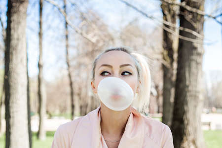Cute young woman with bubble chewing gum outdoors, lifestyle portraitの写真素材