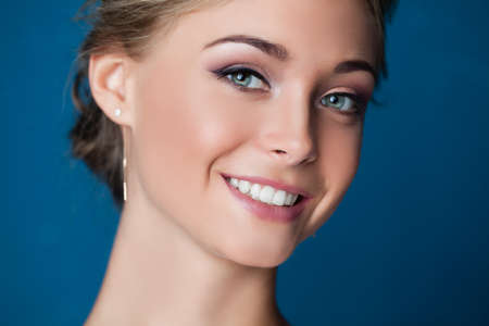Young smiling woman face on blue background, closeup portrait. Cute smileの写真素材
