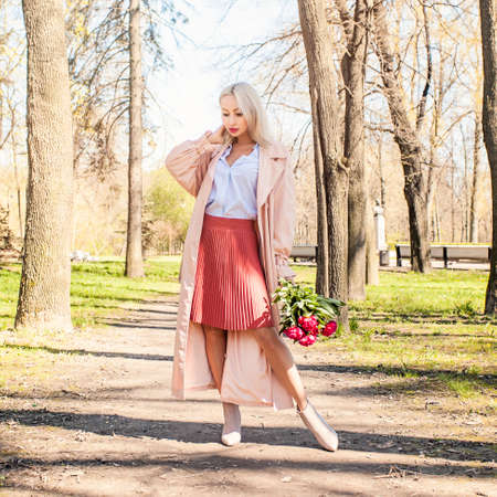 Attractive woman with flowers outdoors. Blonde female model with peony walking in parkの写真素材