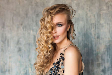 Young Perfect Blonde Woman with Long Wavy Hair and Makeup against Grey Wall Background with Copy spaceの写真素材