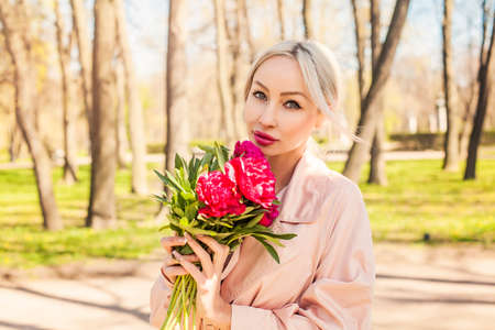 Cheerful blonde woman with peony flowers bunch, outdoors portraitの写真素材