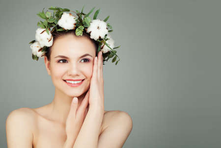 Happy young woman with cotton flowers and green leaves on banner background with copy space. Healthcare, skincare and cosmetology conceptの写真素材