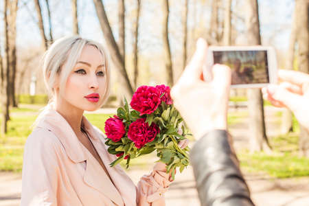 Beautiful woman with peony flowers, outdoors portraitの写真素材
