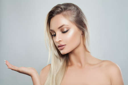 Young Perfect Woman with Natural Makeup, Healthy Skin and Blonde Hair Showing Empty Copy Space on the Open Hand. Facial treatment, Cosmetology, Beauty, Skincare and Spaの写真素材