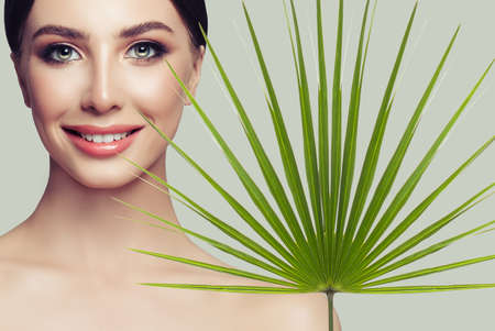 Cheerful spa woman with healthy skin and green palm leaf on grey background. Facial treatment, cosmetology and spa beautyの写真素材