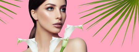 Spa woman with healthy skin, white flowers and tropical leaves on pink background, spa beauty and facial treatmentの写真素材