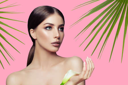 Young woman with healthy skin, green leaves and white flower on pink background. Spa beauty, skincare and wellnessの写真素材