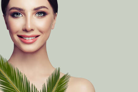 Smiling woman spa model with perfect healthy skin and green leaves on grey background. Facial treatment, cosmetology and spa beautyの写真素材