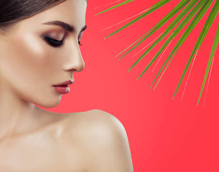 Closeup portrait of perfect spa woman with healthy skin and tropical leaves on redの写真素材