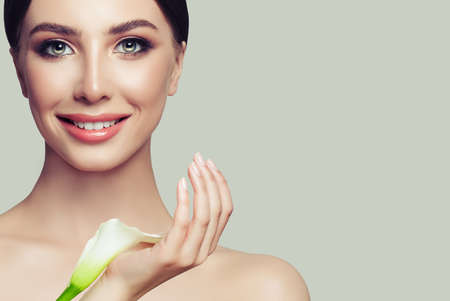 Beautiful young woman with clean fresh skin and white flower. Girl beauty face care. Facial treatment and spa.の写真素材
