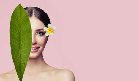 Beautiful woman with healthy skin, tropical leaves and flower on pink backgroundの写真素材